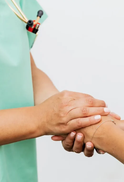 two people clasping hands. Only their arms and hands are visible. We can see one is a medical professional in green scrubs