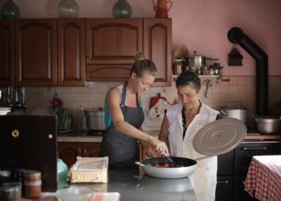 two women preparing a meal, one of them is stirring in a large pan