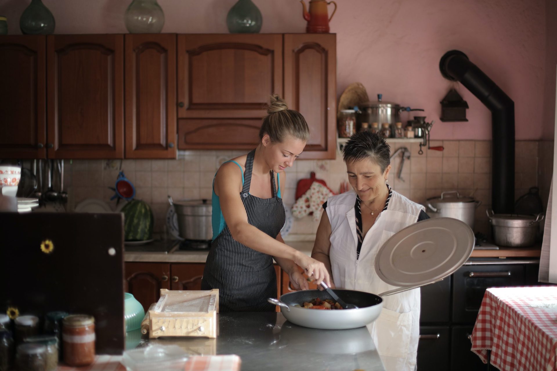 two women preparing a meal, one of them is stirring in a large pan