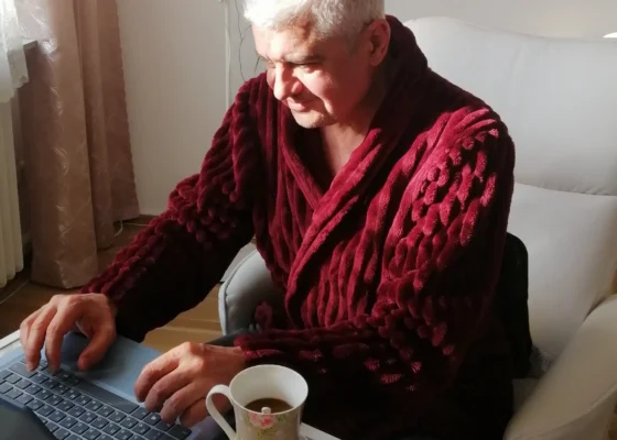 an older man wearing a red robe sat at a laptop