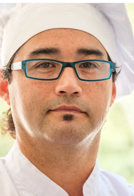 Man in black glasses looking at the camera.He is wearing chefs whites.