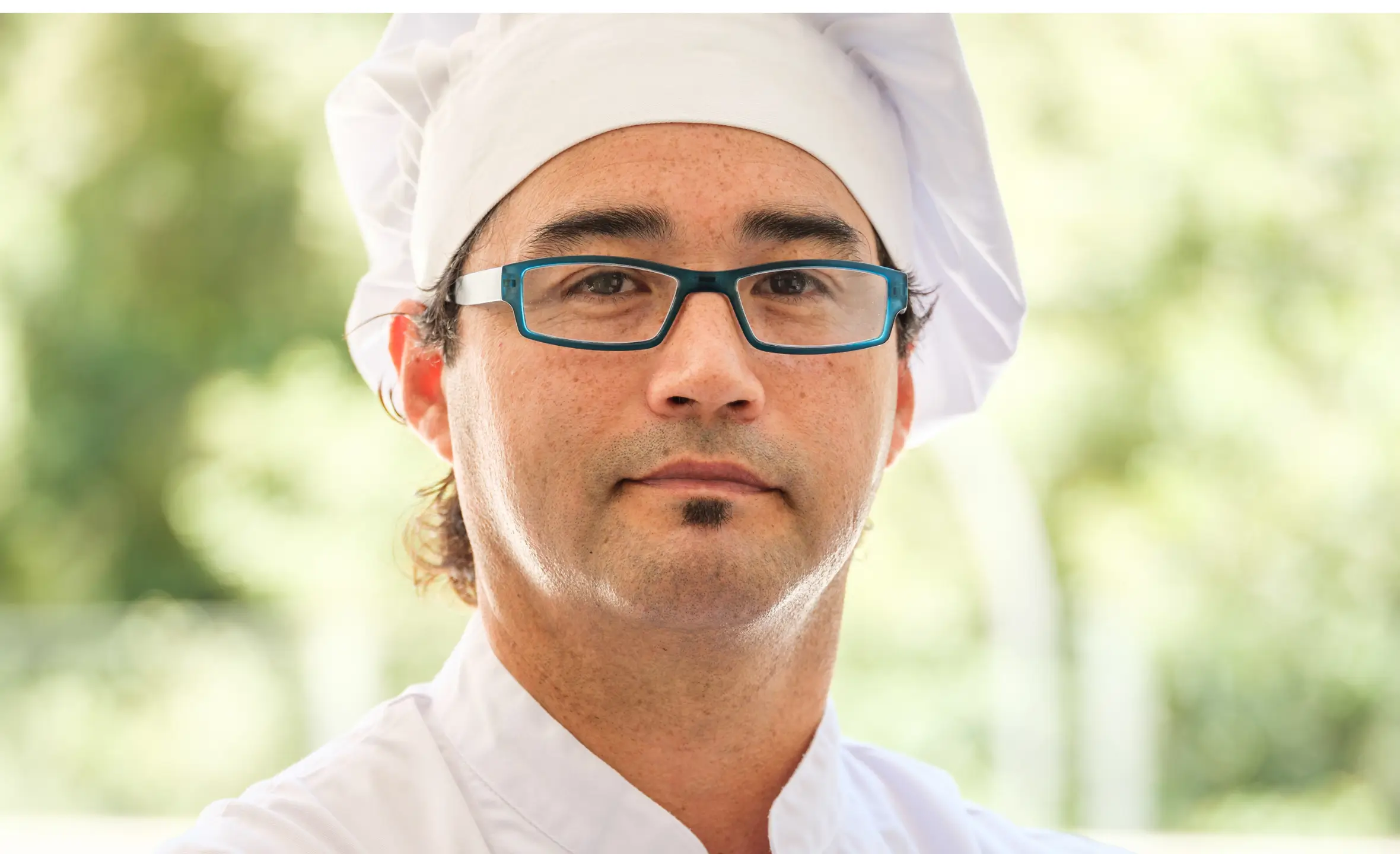 Man in black glasses looking at the camera.He is wearing chefs whites.