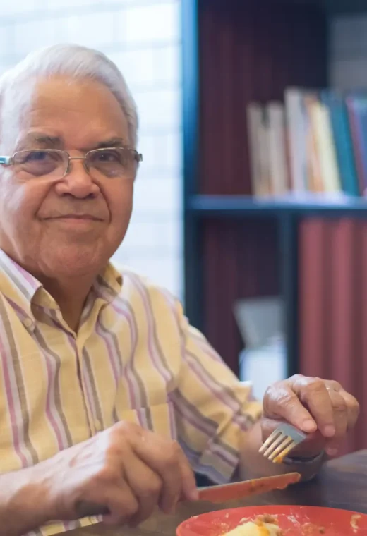 an older gentleman eating a meal while looking into the camera and smiling