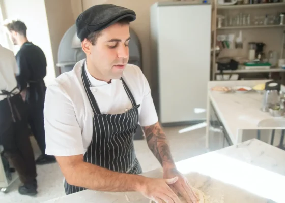 a man wearing a white chef top and a blue apron is preparing food.