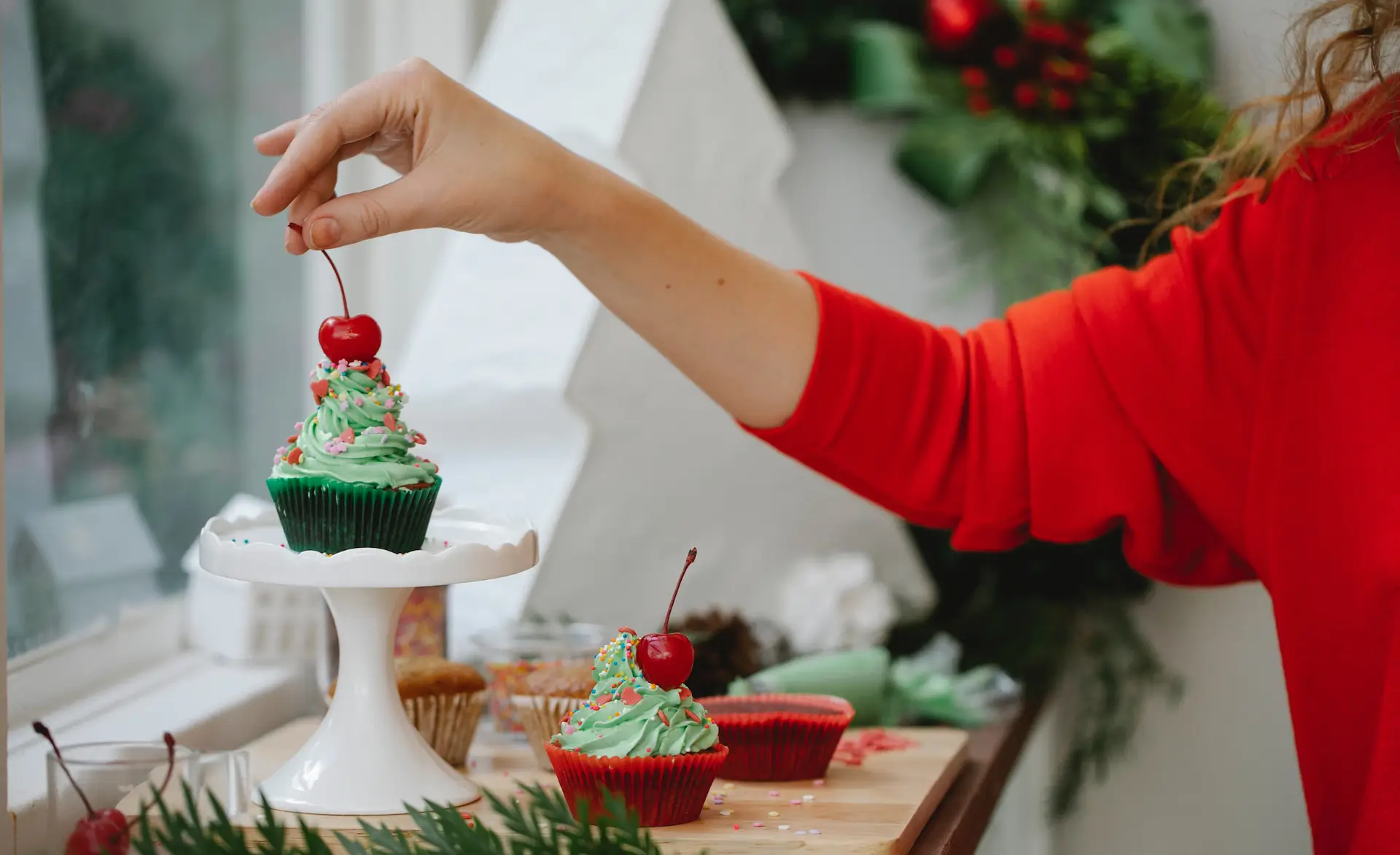 image of a hand putting a cherry on top of a Christmas themed cupcake