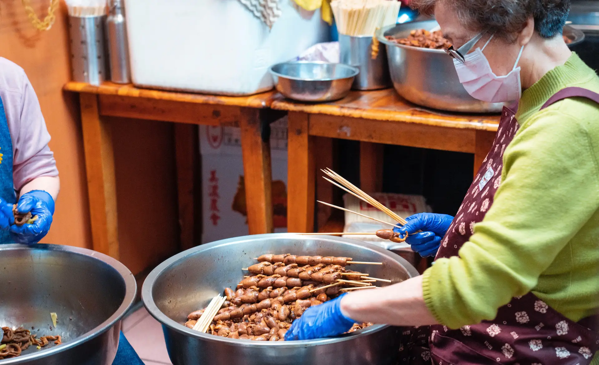 lady stood over a large cooking pot making a type of kebab skewer