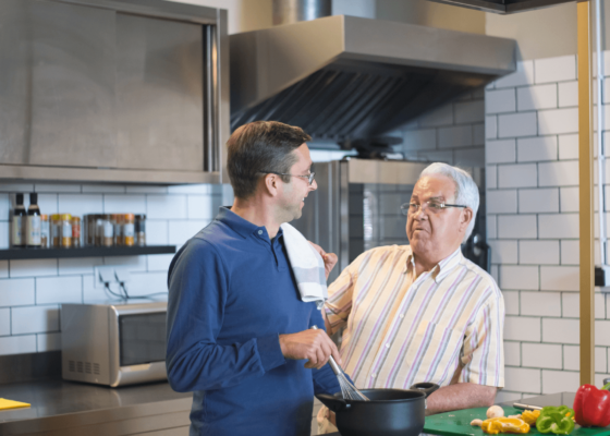 2 men cooking together, they are smiling and enjoying themselves