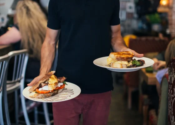 a man wearing black holding two plates of food