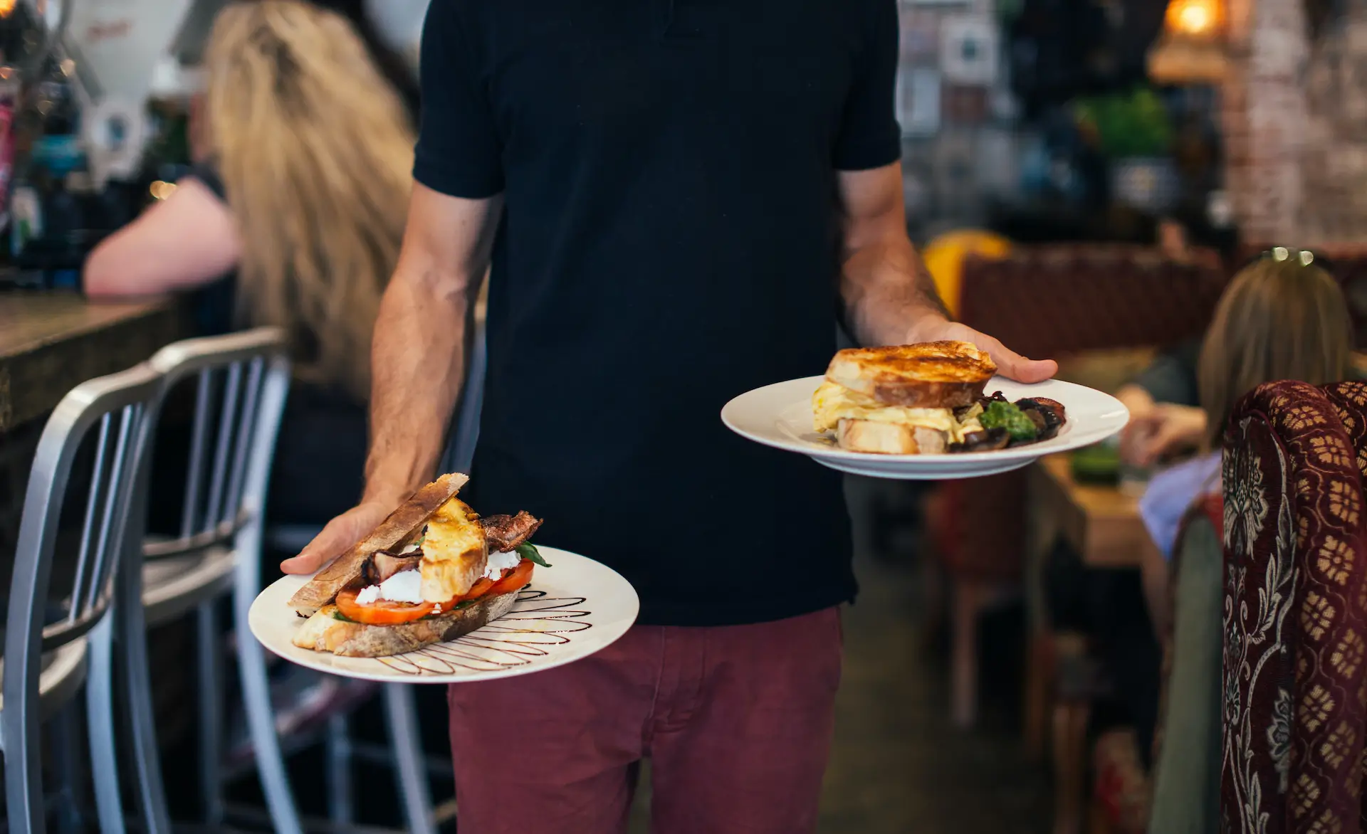 a man wearing black holding two plates of food