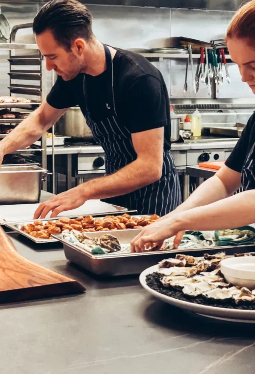 two caterers in a kitchen preparing meals in multiple dishes