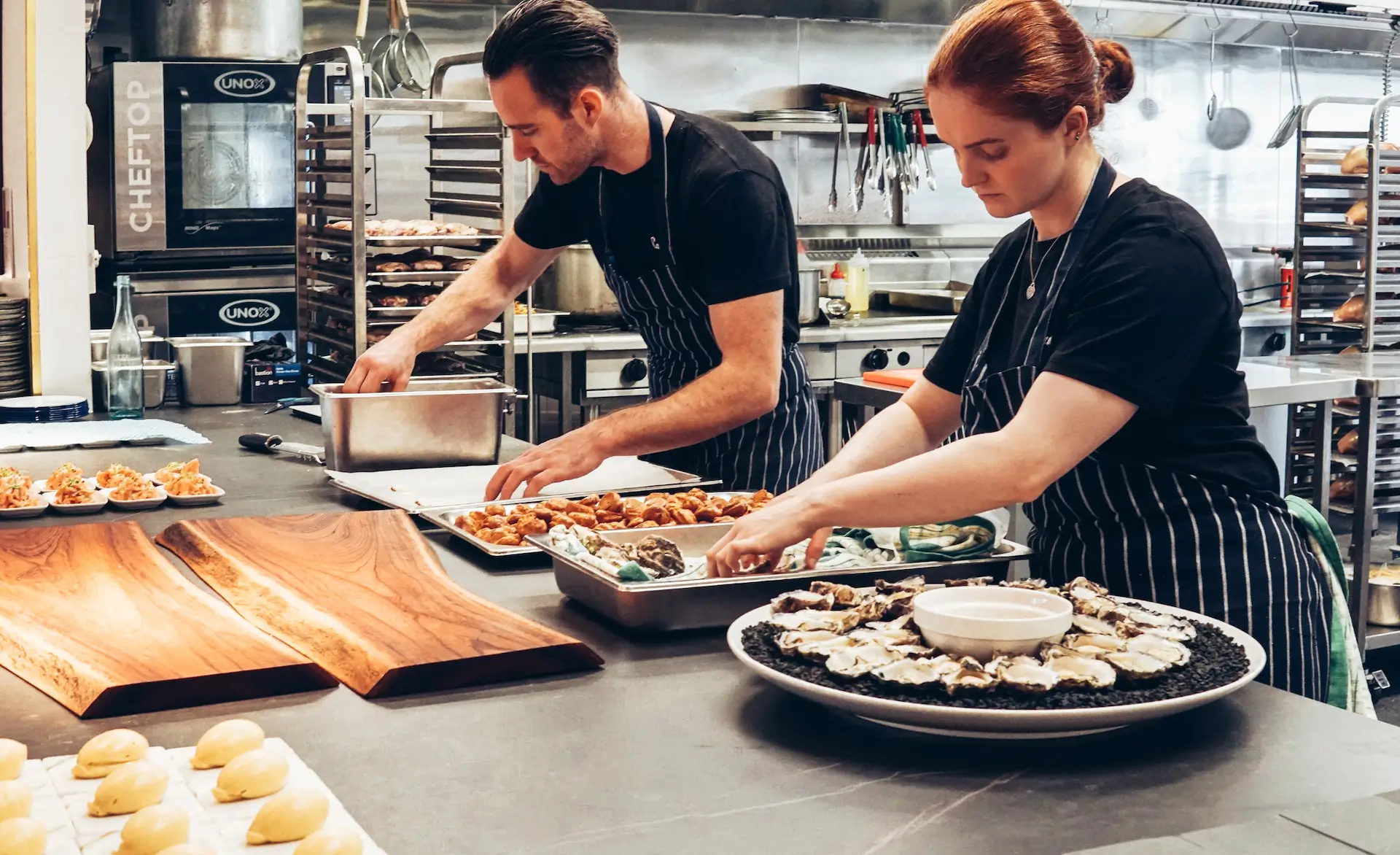 two caterers in a kitchen preparing meals in multiple dishes