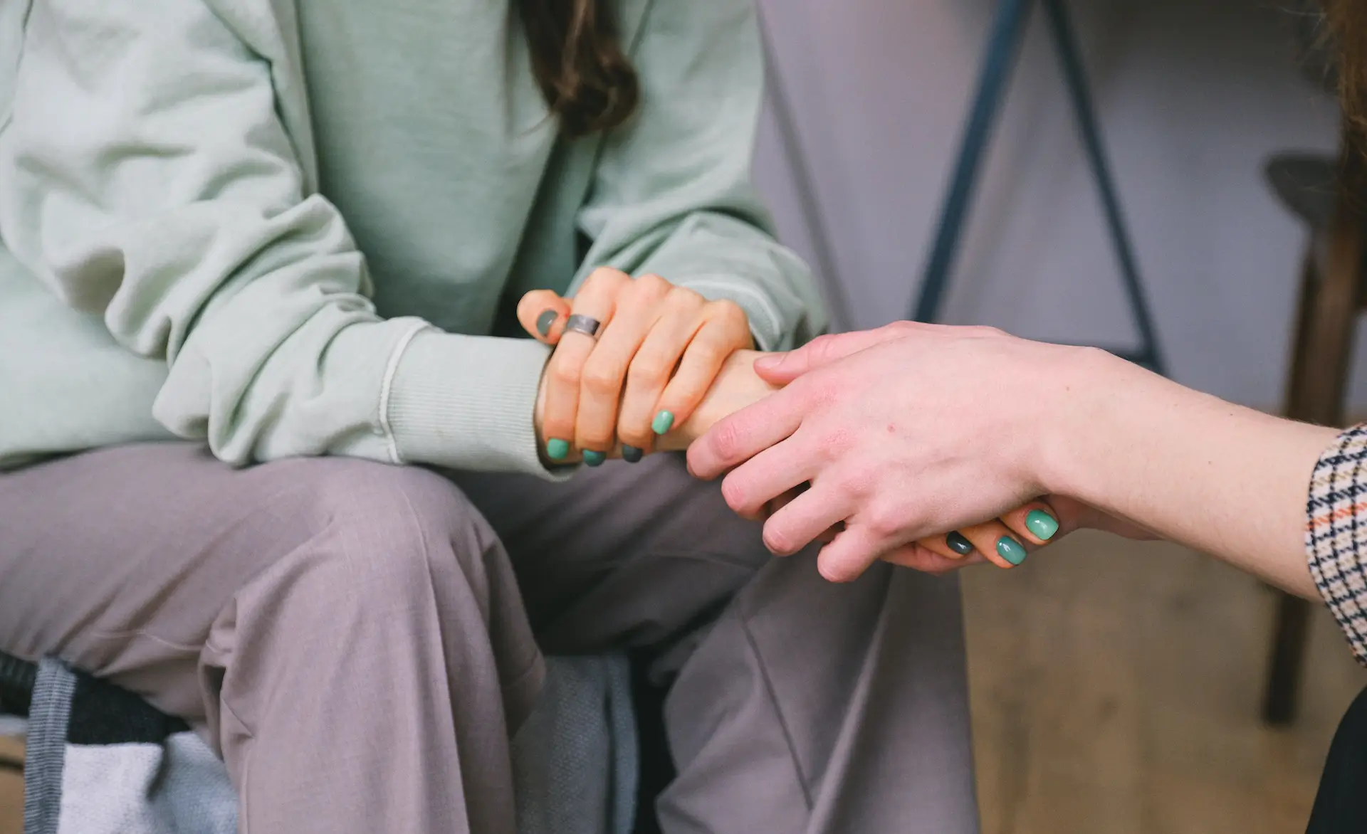 two people sat together. One is wearing hospital scrubs and is holding the hand of the other person