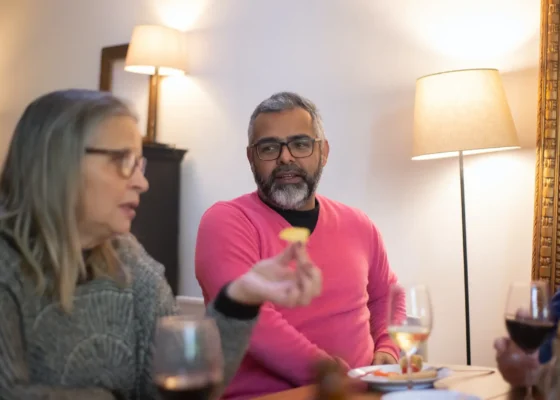 a man and woman sat at a table eating food with glasses of wine