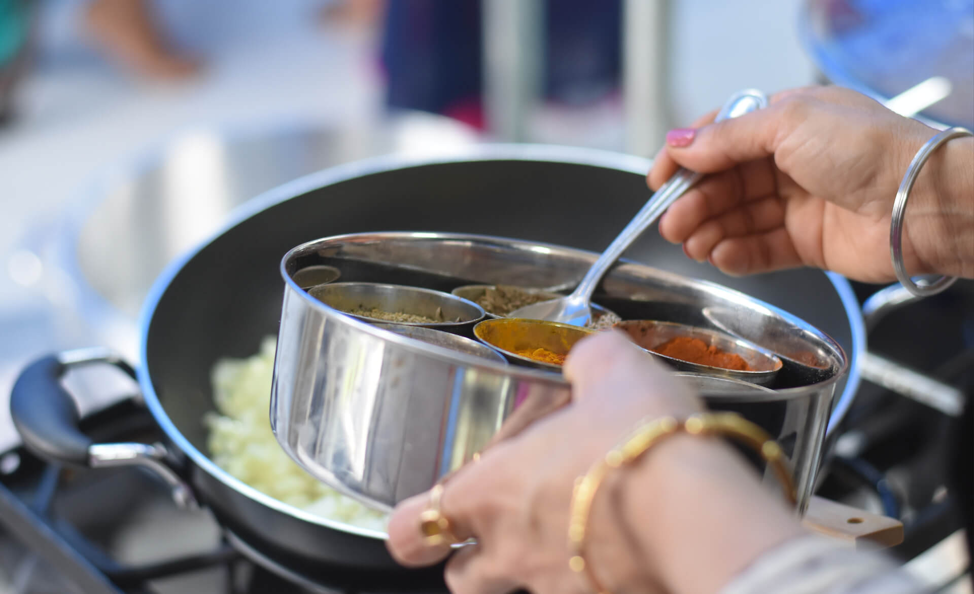 a close up of a person putting spices into a pot of food in the public sector catering industry